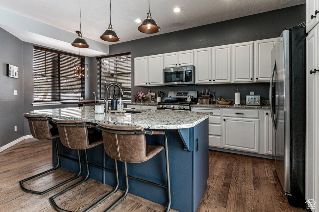 Kitchen with appliances with stainless steel finishes, pendant lighting, white cabinets, and an island with sink