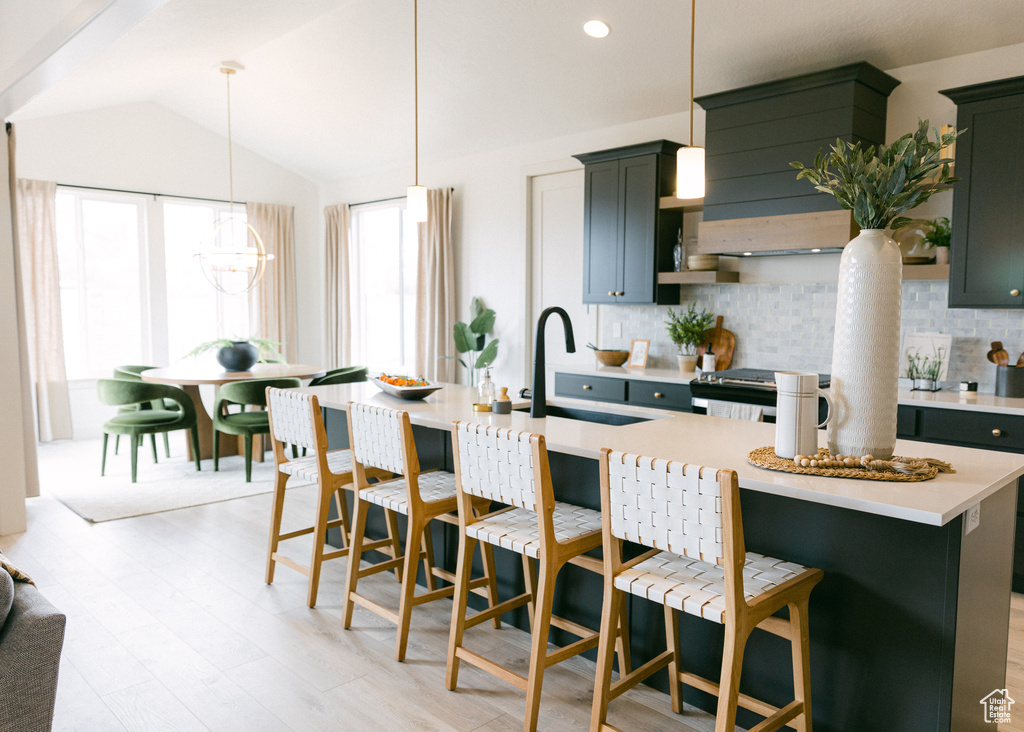 Kitchen featuring a kitchen island with sink, pendant lighting, vaulted ceiling, sink, and backsplash