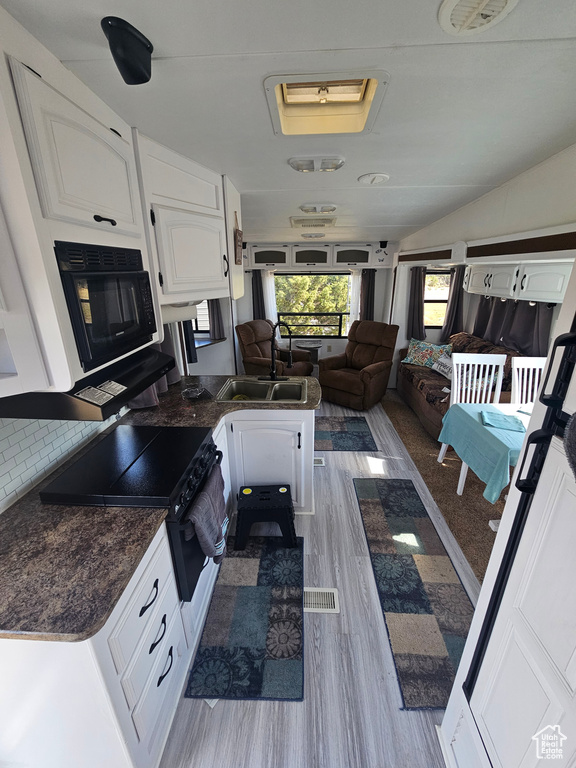 Kitchen with kitchen peninsula, light hardwood / wood-style floors, sink, and white cabinetry