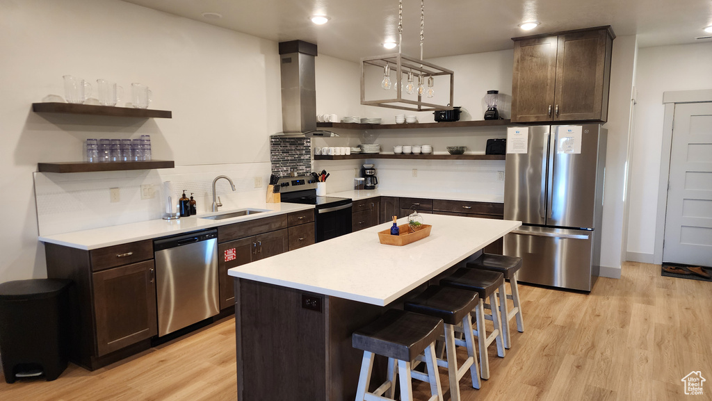 Kitchen with light wood-type flooring, range hood, sink, appliances with stainless steel finishes, and a kitchen bar