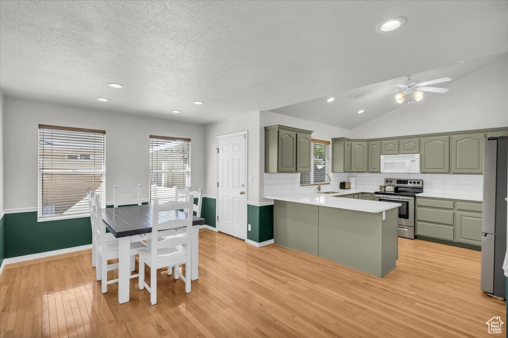 Kitchen featuring light hardwood / wood-style floors, sink, lofted ceiling, kitchen peninsula, and appliances with stainless steel finishes