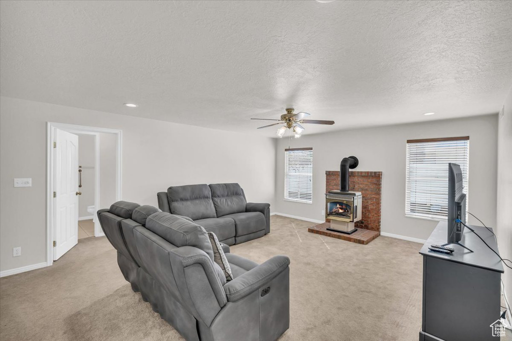 Carpeted living room with a textured ceiling, ceiling fan, a wealth of natural light, and a wood stove