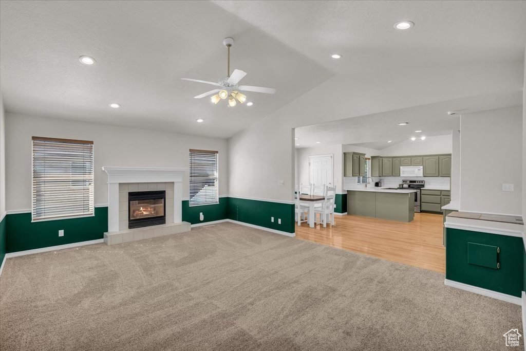 Living room with light carpet, ceiling fan, vaulted ceiling, and a tiled fireplace