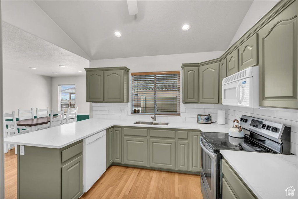 Kitchen with white appliances, light hardwood / wood-style flooring, lofted ceiling, kitchen peninsula, and backsplash