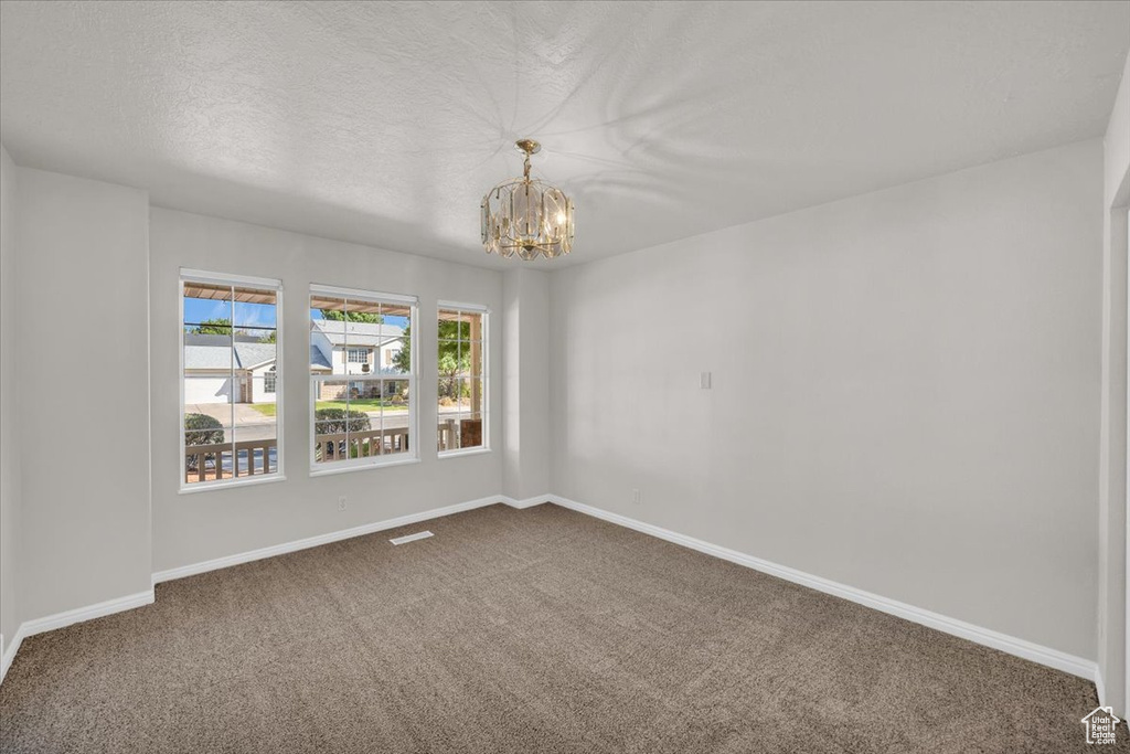 Spare room featuring a notable chandelier, a textured ceiling, and carpet