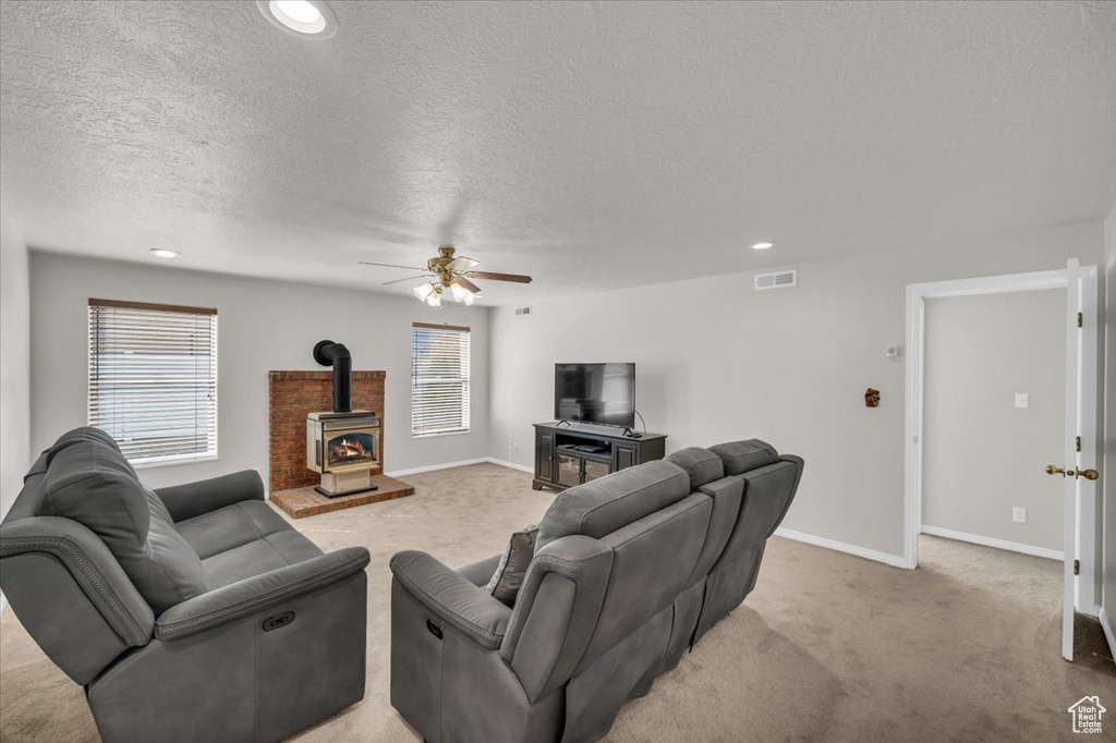 Living room featuring ceiling fan, light colored carpet, and a wood stove