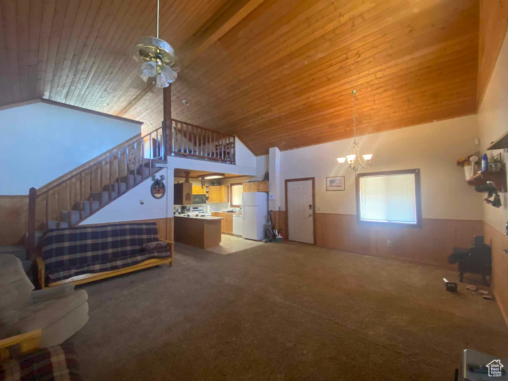 Carpeted living room featuring ceiling fan with notable chandelier, wooden walls, wood ceiling, and high vaulted ceiling