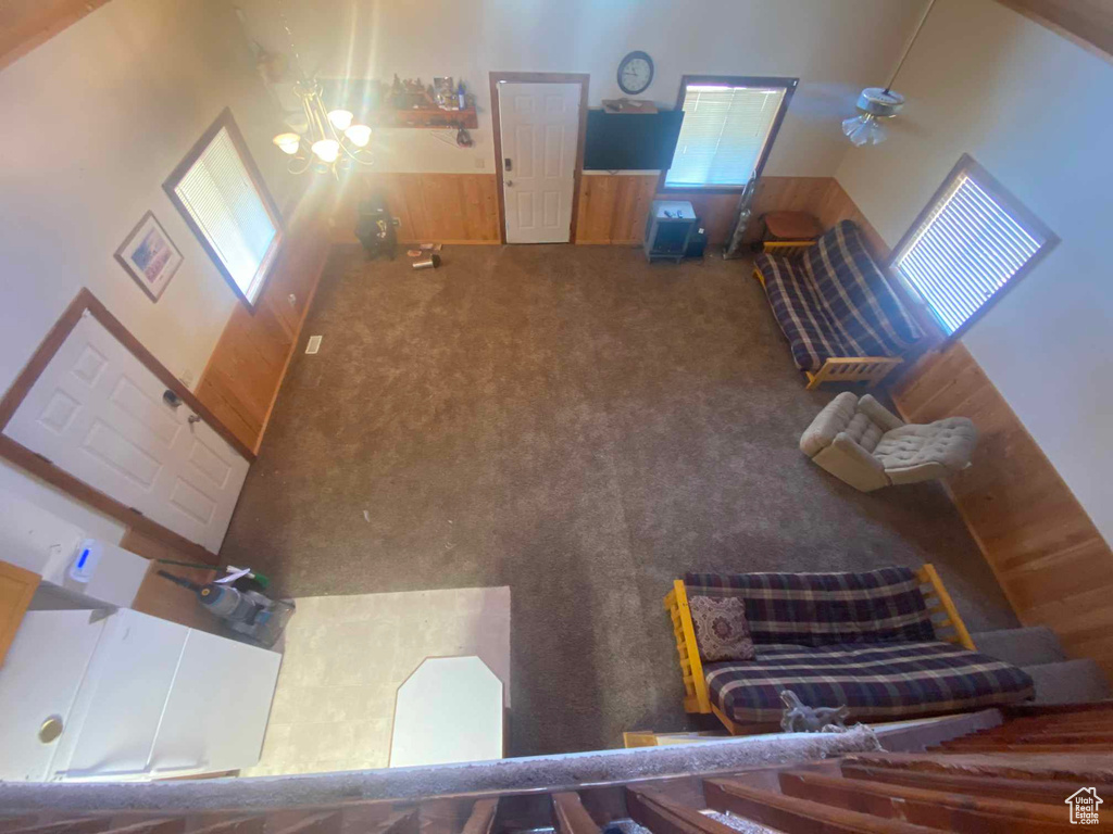 Carpeted living room featuring high vaulted ceiling, wooden walls, and a chandelier