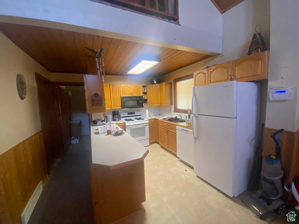 Kitchen with sink, wooden walls, white appliances, and wooden ceiling