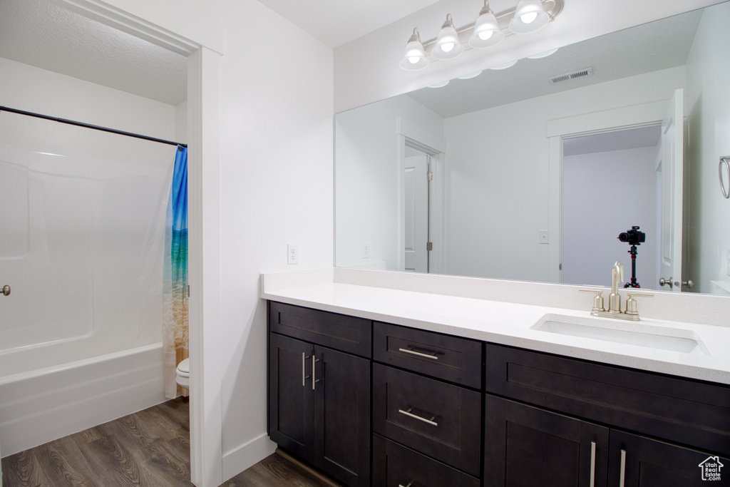 Full bathroom featuring hardwood / wood-style flooring, shower / bath combo, vanity, and toilet