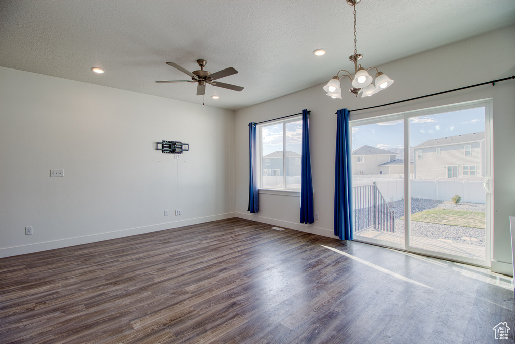 Empty room with ceiling fan with notable chandelier, dark hardwood / wood-style floors, and a textured ceiling