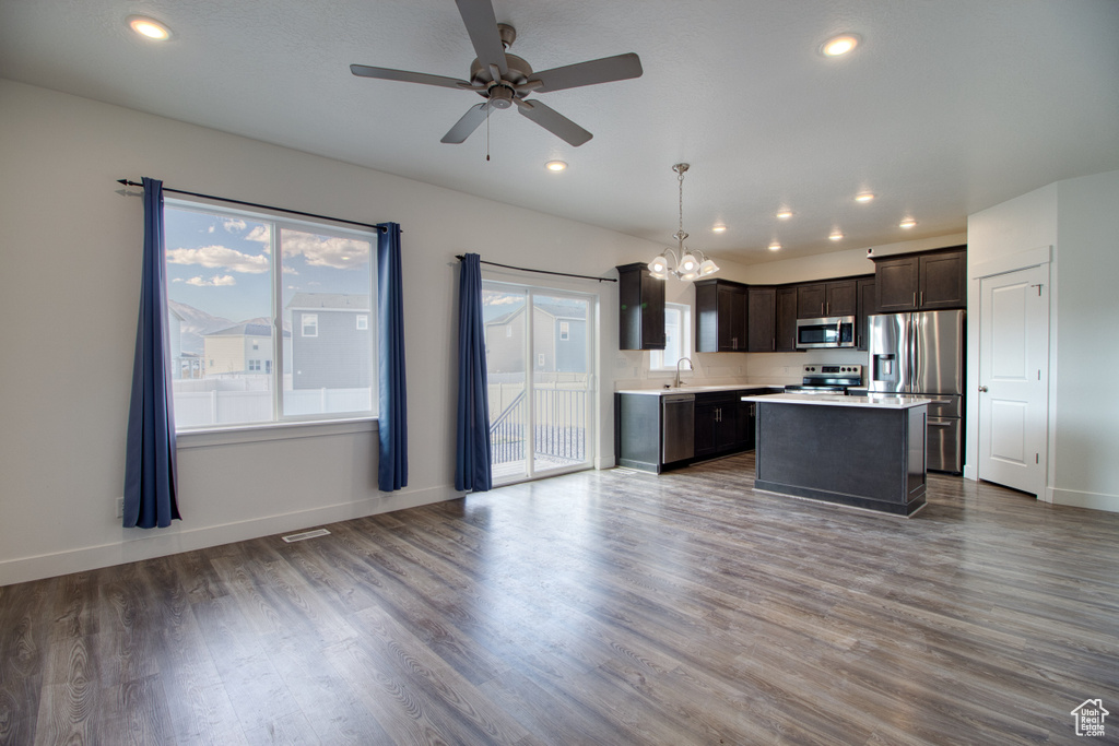 Kitchen featuring dark brown cabinetry, a kitchen island, decorative light fixtures, stainless steel appliances, and dark hardwood / wood-style floors