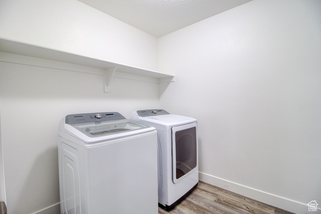 Washroom with a textured ceiling, washer and clothes dryer, and light hardwood / wood-style flooring