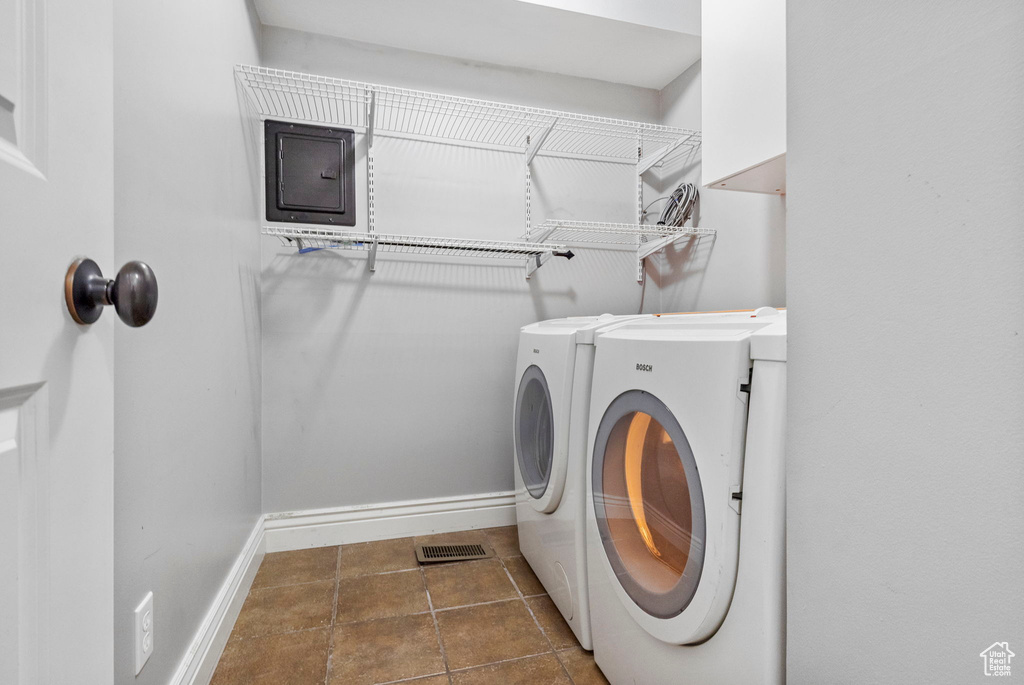 Washroom with electric panel, dark tile patterned flooring, and washing machine and clothes dryer