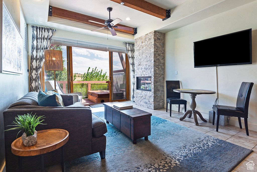 Living room featuring a fireplace, beam ceiling, light tile patterned floors, and ceiling fan