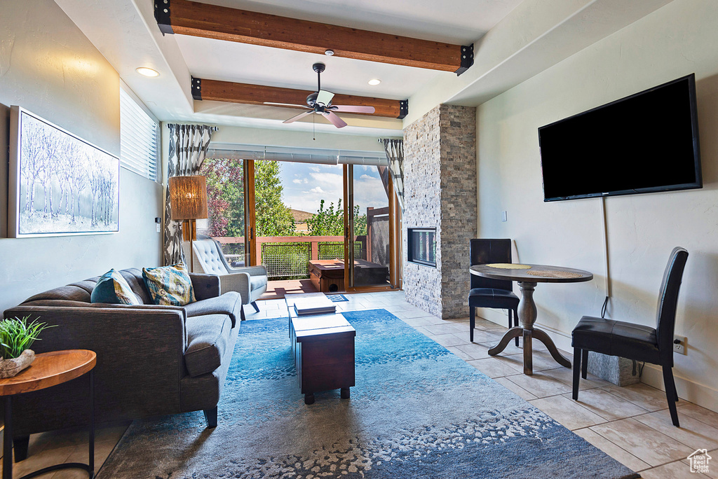 Living room featuring ceiling fan, light tile patterned flooring, a fireplace, and beam ceiling