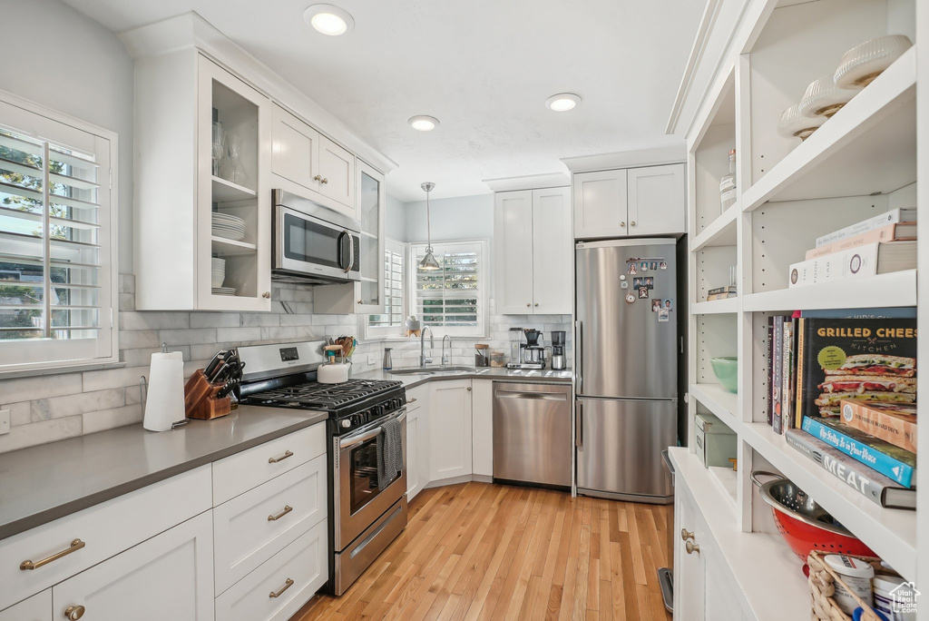 Kitchen featuring light wood-type flooring, decorative light fixtures, sink, white cabinets, and appliances with stainless steel finishes