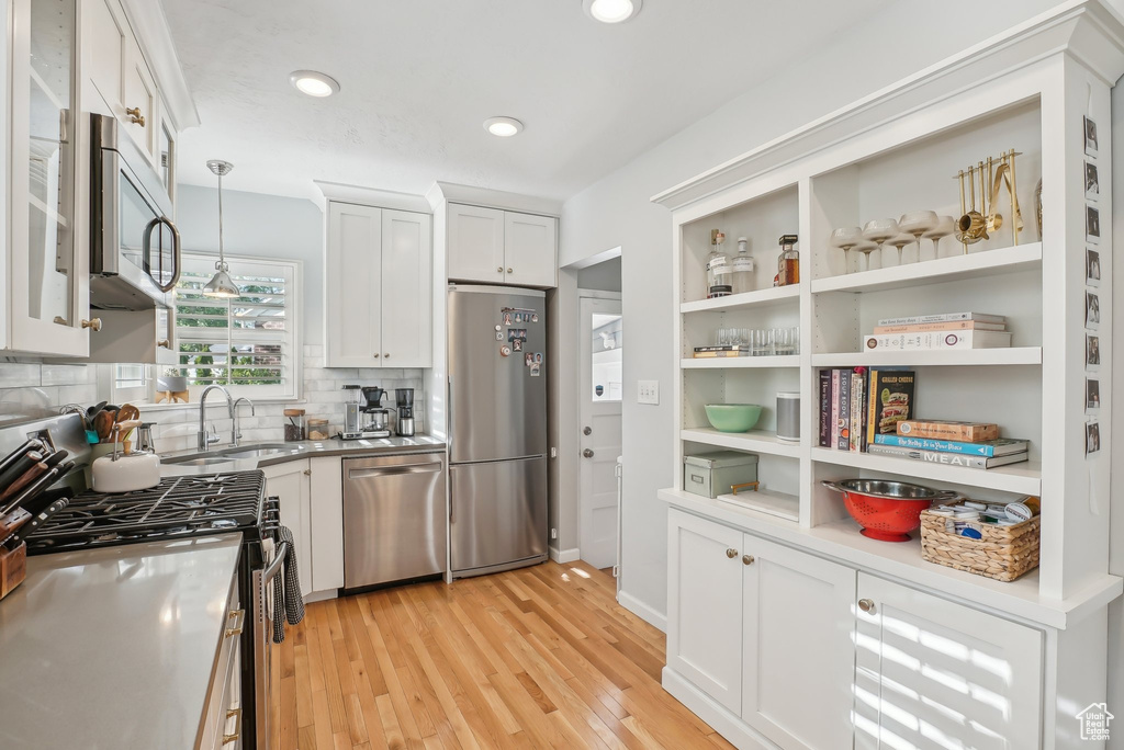 Kitchen featuring pendant lighting, stainless steel appliances, light hardwood / wood-style floors, and white cabinetry