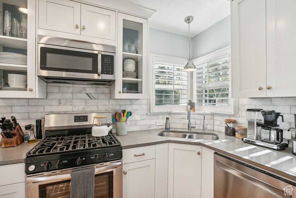 Kitchen featuring stainless steel appliances, white cabinets, sink, pendant lighting, and backsplash