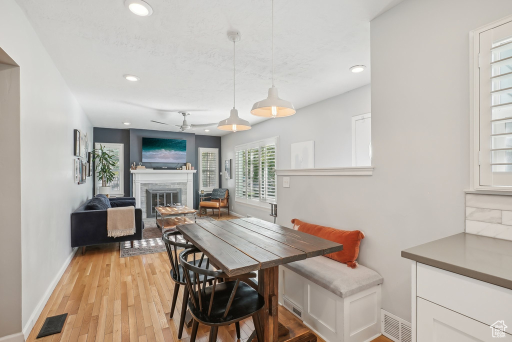 Dining space with ceiling fan, light wood-type flooring, and a fireplace