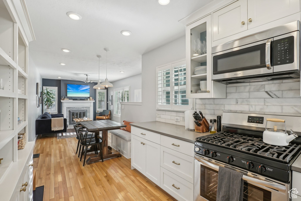 Kitchen featuring white cabinets, stainless steel appliances, decorative light fixtures, and light hardwood / wood-style flooring