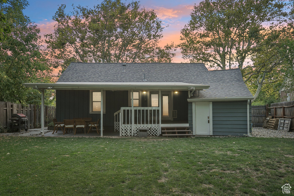 Back house at dusk with a patio and a lawn