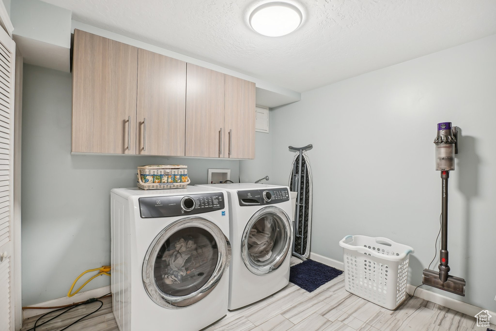 Laundry room with light hardwood / wood-style floors, cabinets, and washer and clothes dryer