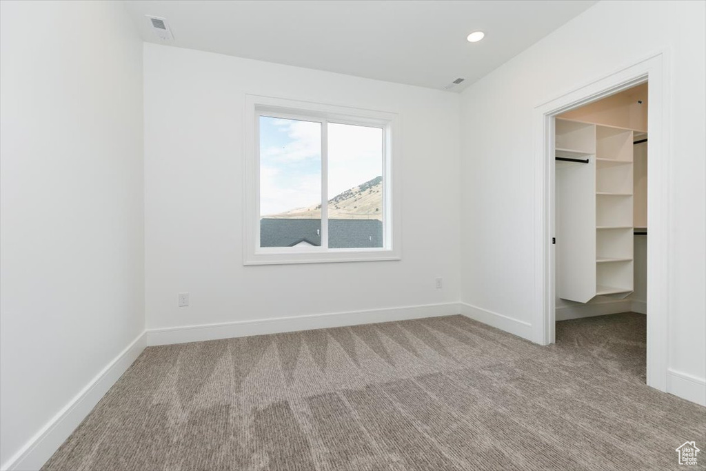 Unfurnished bedroom featuring light colored carpet and a walk in closet