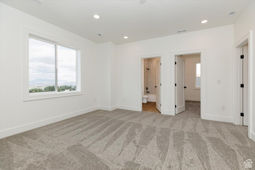 Unfurnished bedroom featuring light carpet, connected bathroom, and a walk in closet