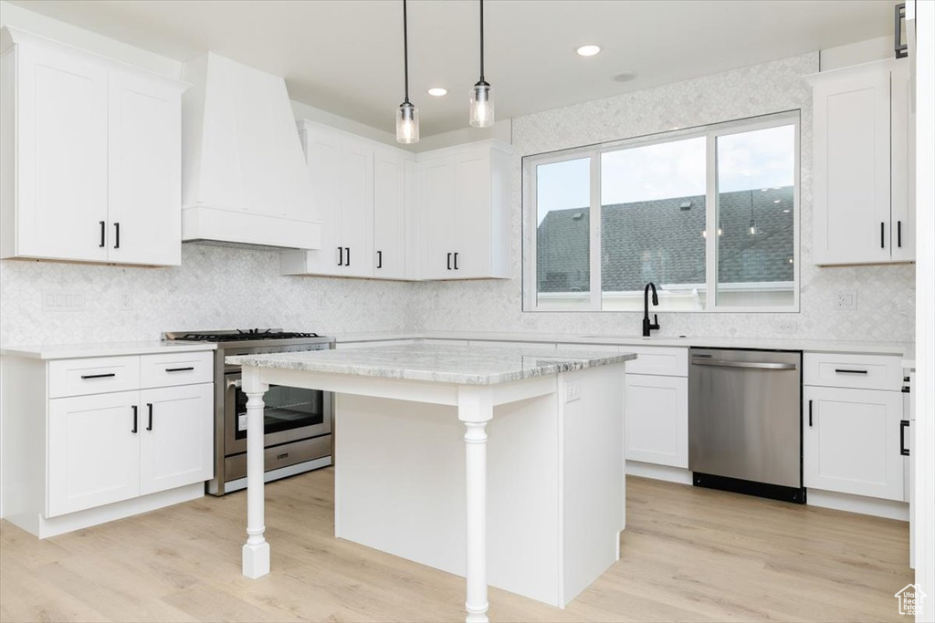 Kitchen featuring white cabinets, stainless steel appliances, hanging light fixtures, and custom range hood