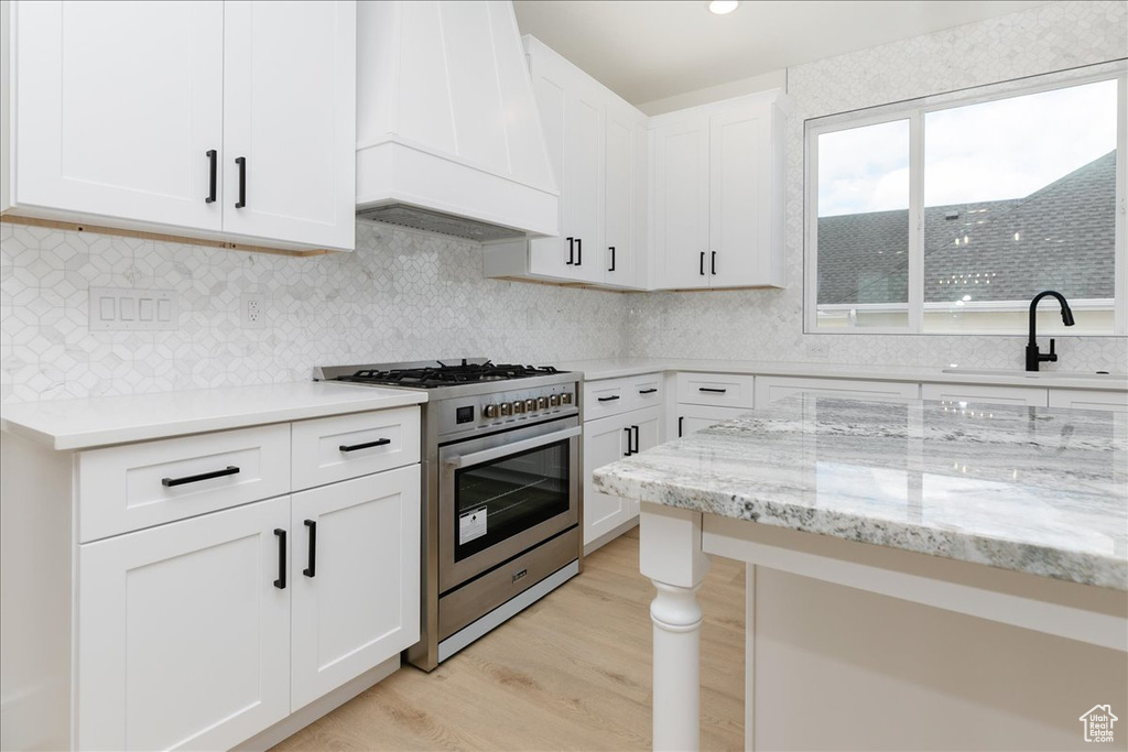 Kitchen featuring high end stainless steel range oven, sink, white cabinetry, light hardwood / wood-style flooring, and custom exhaust hood