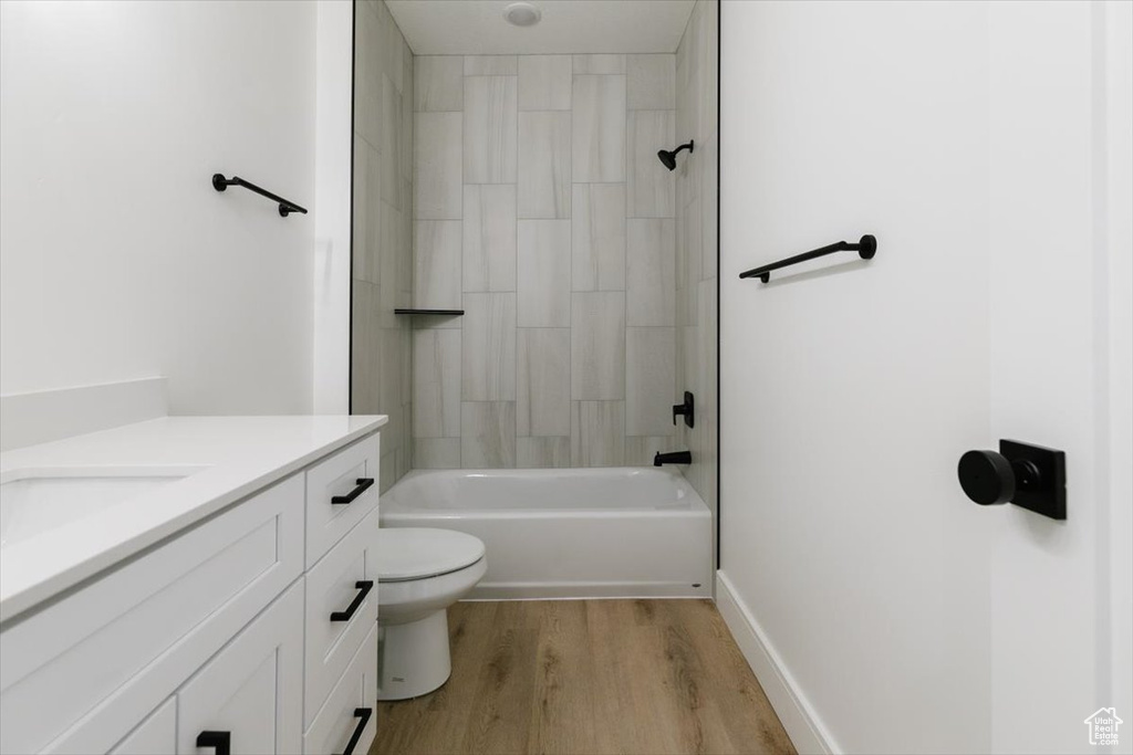 Full bathroom with tiled shower / bath, vanity, hardwood / wood-style floors, and toilet