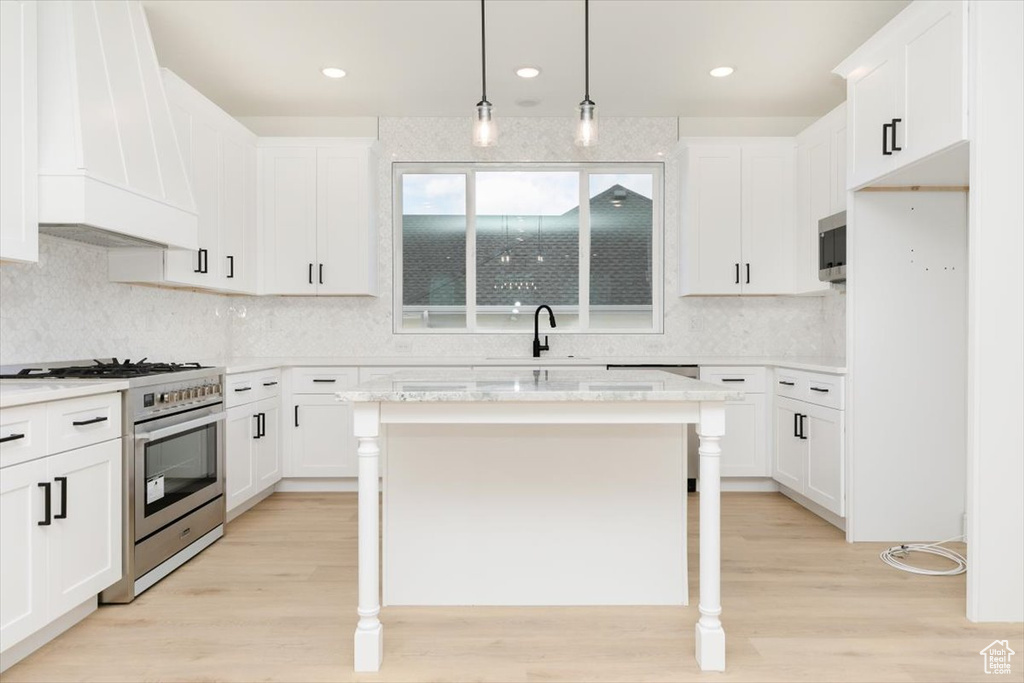 Kitchen featuring a center island, hanging light fixtures, light hardwood / wood-style flooring, appliances with stainless steel finishes, and custom exhaust hood