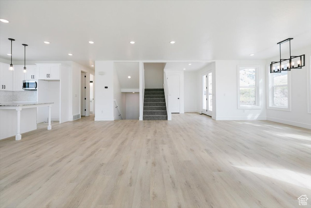 Unfurnished living room featuring an inviting chandelier and light hardwood / wood-style flooring