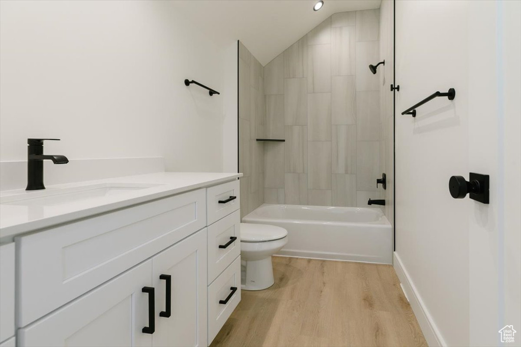 Full bathroom with toilet, wood-type flooring, vaulted ceiling, tiled shower / bath combo, and vanity