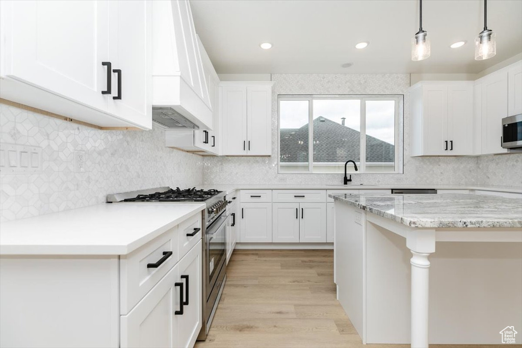 Kitchen with light hardwood / wood-style flooring, decorative light fixtures, stainless steel appliances, light stone countertops, and white cabinetry