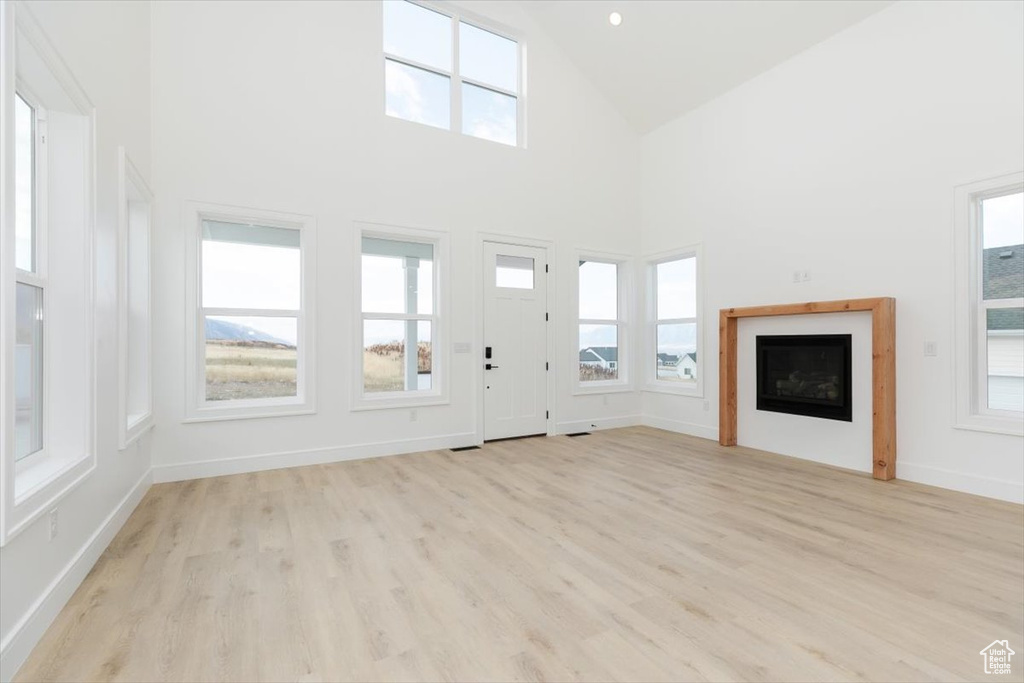 Unfurnished living room with light hardwood / wood-style floors and high vaulted ceiling