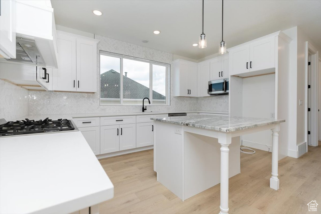 Kitchen with stainless steel appliances, hanging light fixtures, a center island, and white cabinetry