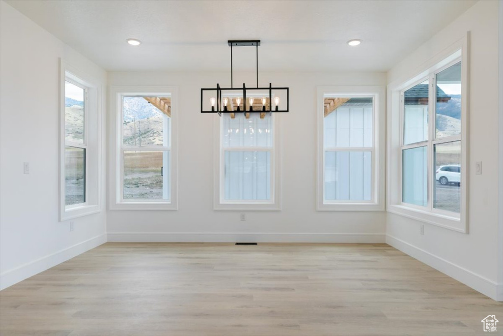 Unfurnished dining area featuring an inviting chandelier and light wood-type flooring