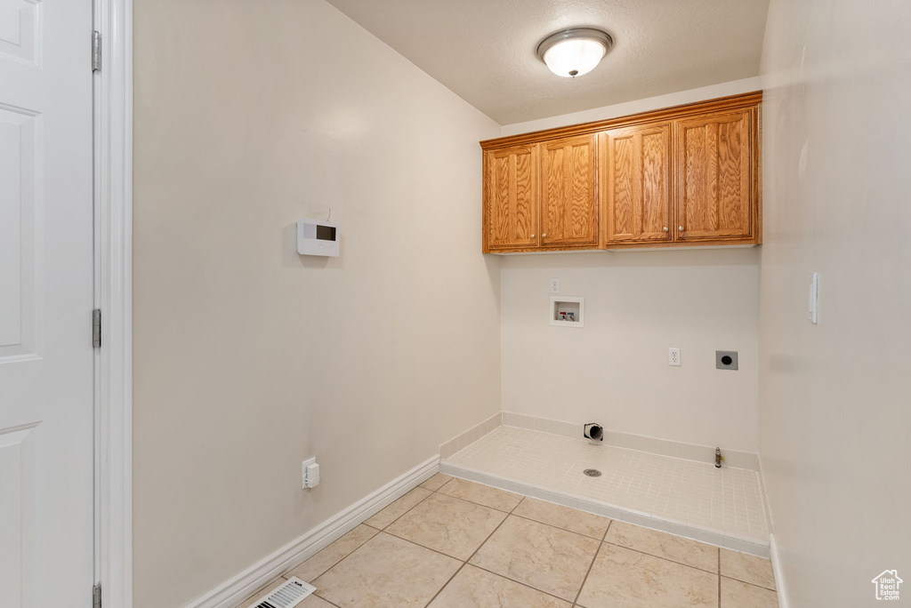 Clothes washing area featuring hookup for an electric dryer, washer hookup, gas dryer hookup, cabinets, and light tile patterned floors