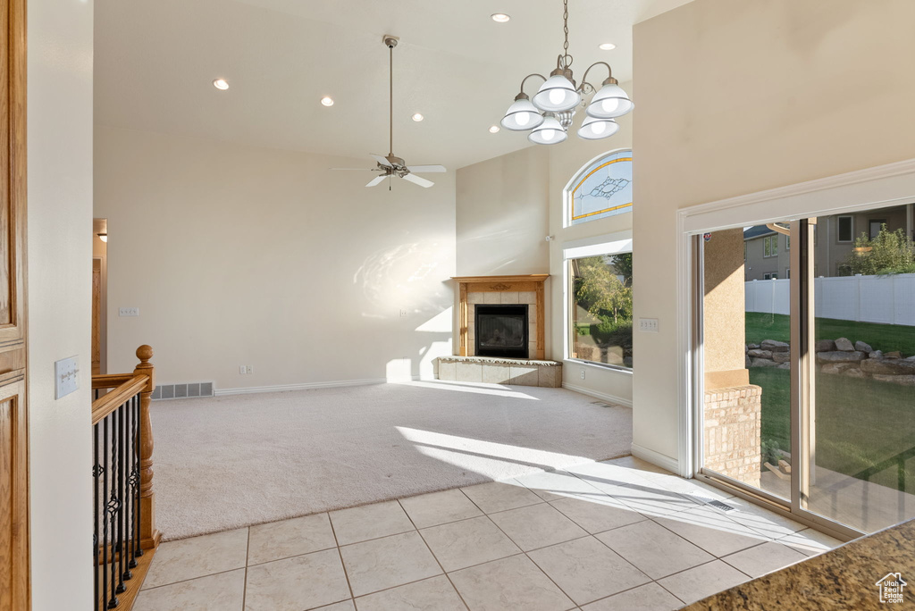 Unfurnished living room with light carpet, ceiling fan with notable chandelier, a fireplace, and a towering ceiling