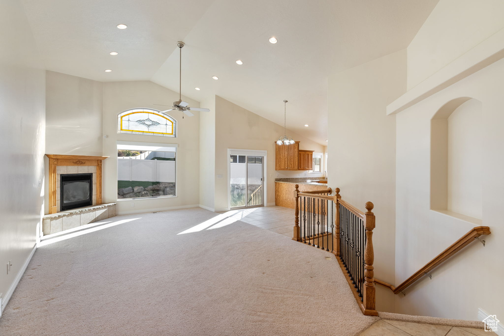 Living room with light carpet, ceiling fan with notable chandelier, a tiled fireplace, and high vaulted ceiling