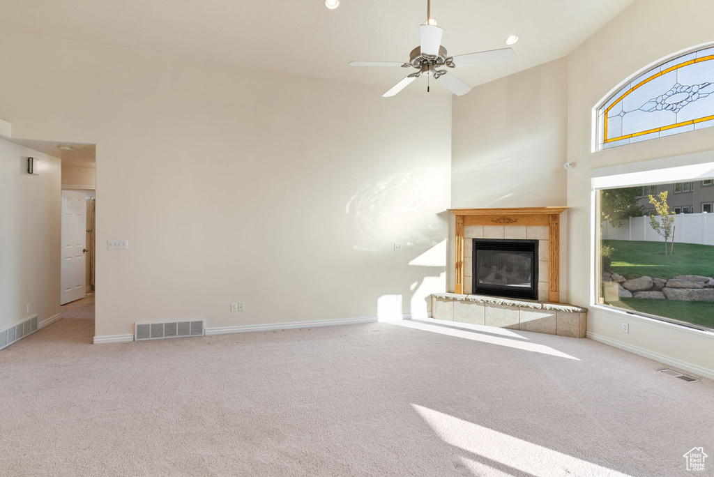 Unfurnished living room with ceiling fan, a high ceiling, carpet flooring, and a tiled fireplace