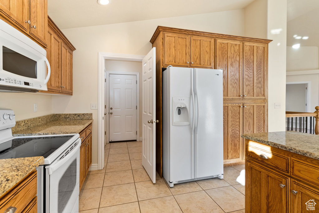 Kitchen featuring light stone countertops, white appliances, and vaulted ceiling