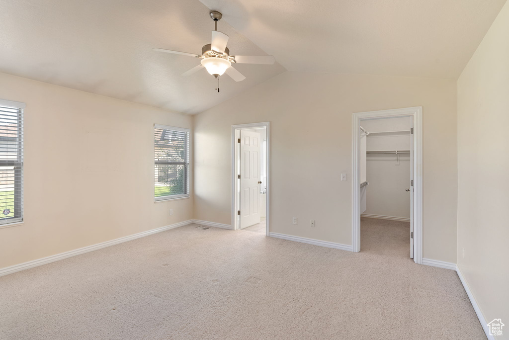 Unfurnished bedroom with a spacious closet, a closet, light colored carpet, and ceiling fan