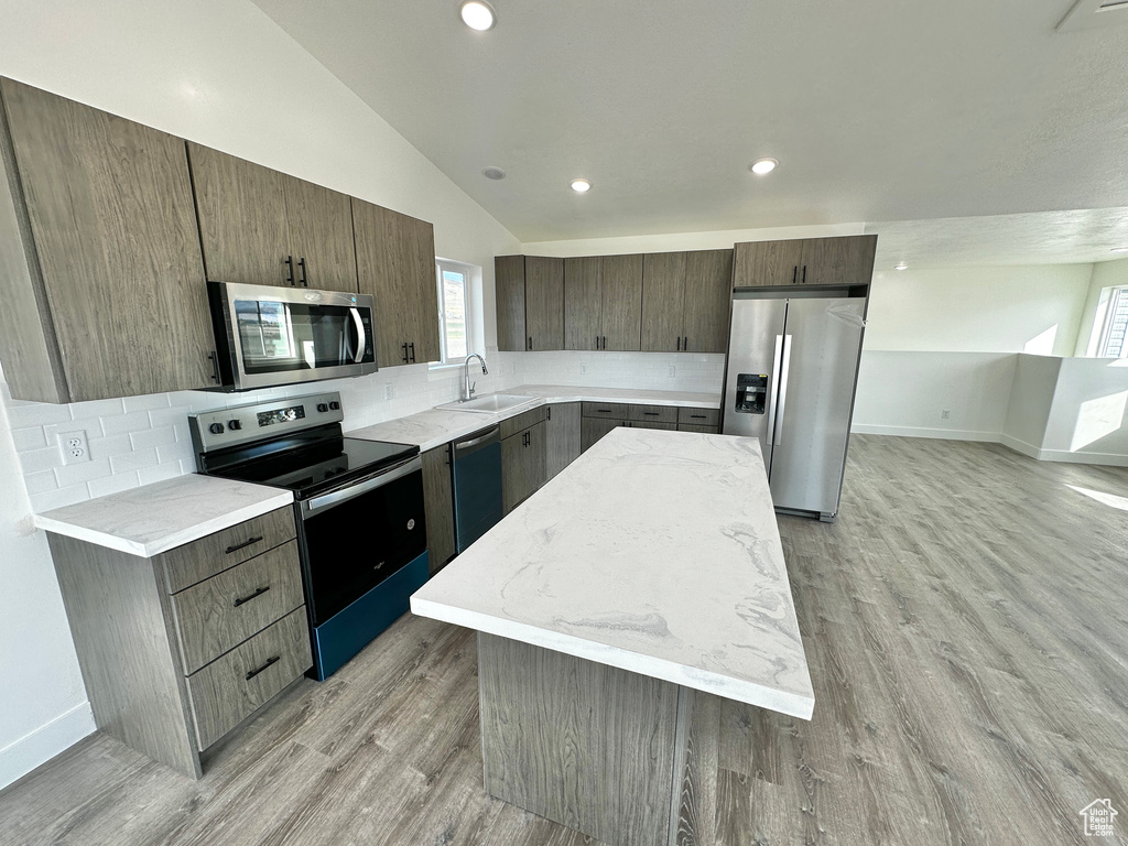 Kitchen featuring a kitchen island, light hardwood / wood-style flooring, vaulted ceiling, sink, and appliances with stainless steel finishes