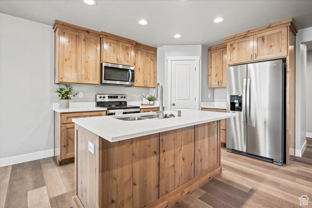 Kitchen with stainless steel appliances, a kitchen island with sink, light hardwood / wood-style flooring, and sink