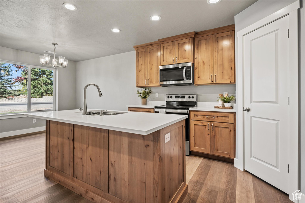 Kitchen featuring appliances with stainless steel finishes, a kitchen island with sink, sink, and decorative light fixtures