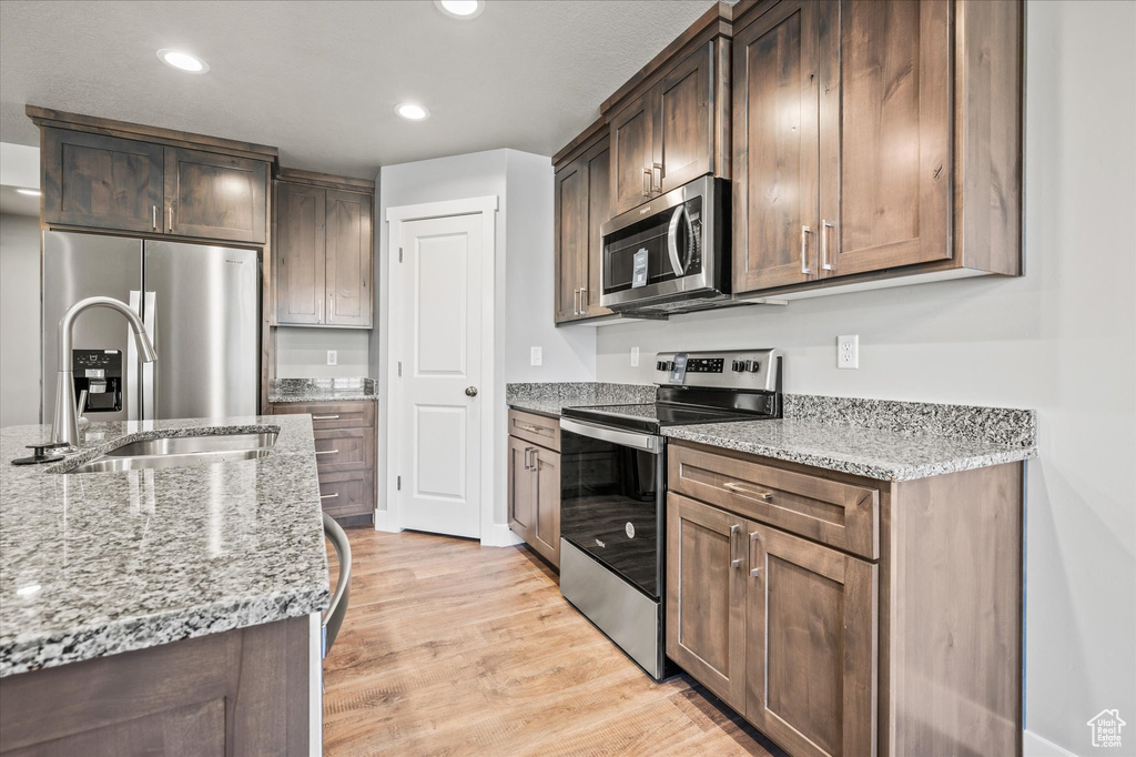 Kitchen with light stone counters, appliances with stainless steel finishes, light wood-type flooring, and dark brown cabinets