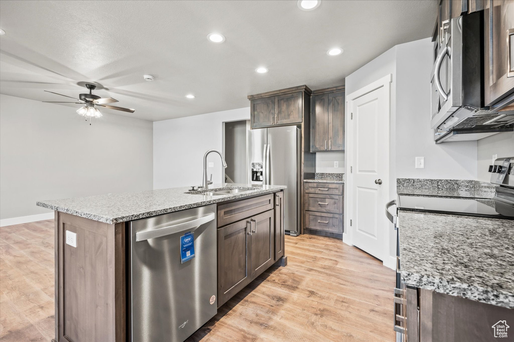 Kitchen featuring an island with sink, light stone countertops, stainless steel appliances, sink, and light hardwood / wood-style floors